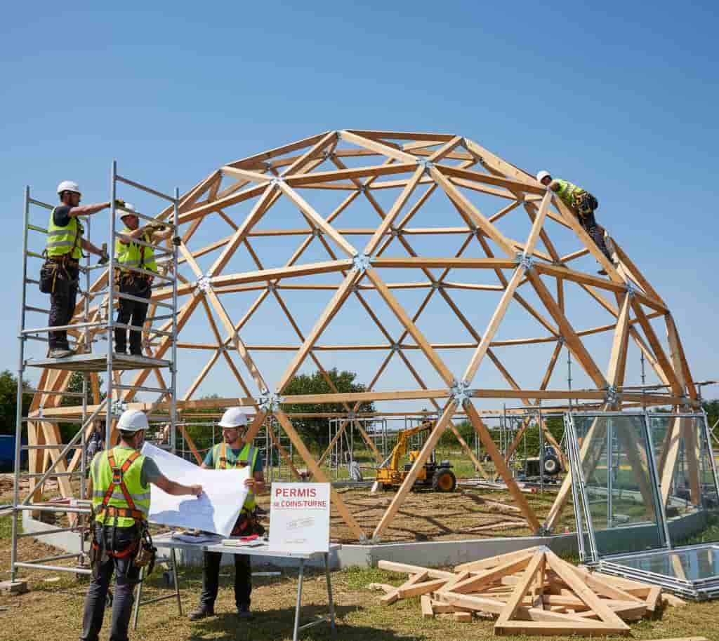 Construction d’un dôme géodésique habitable avec ouvriers assemblant la structure triangulée